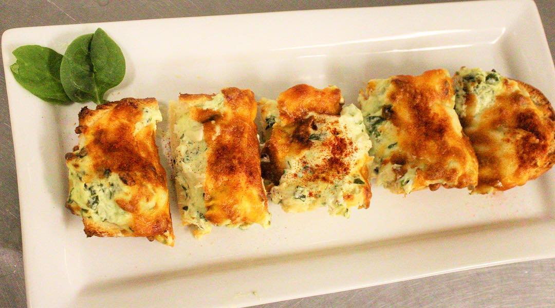 Golden-brown baked rolls filled with herbs and cheese on a white platter.