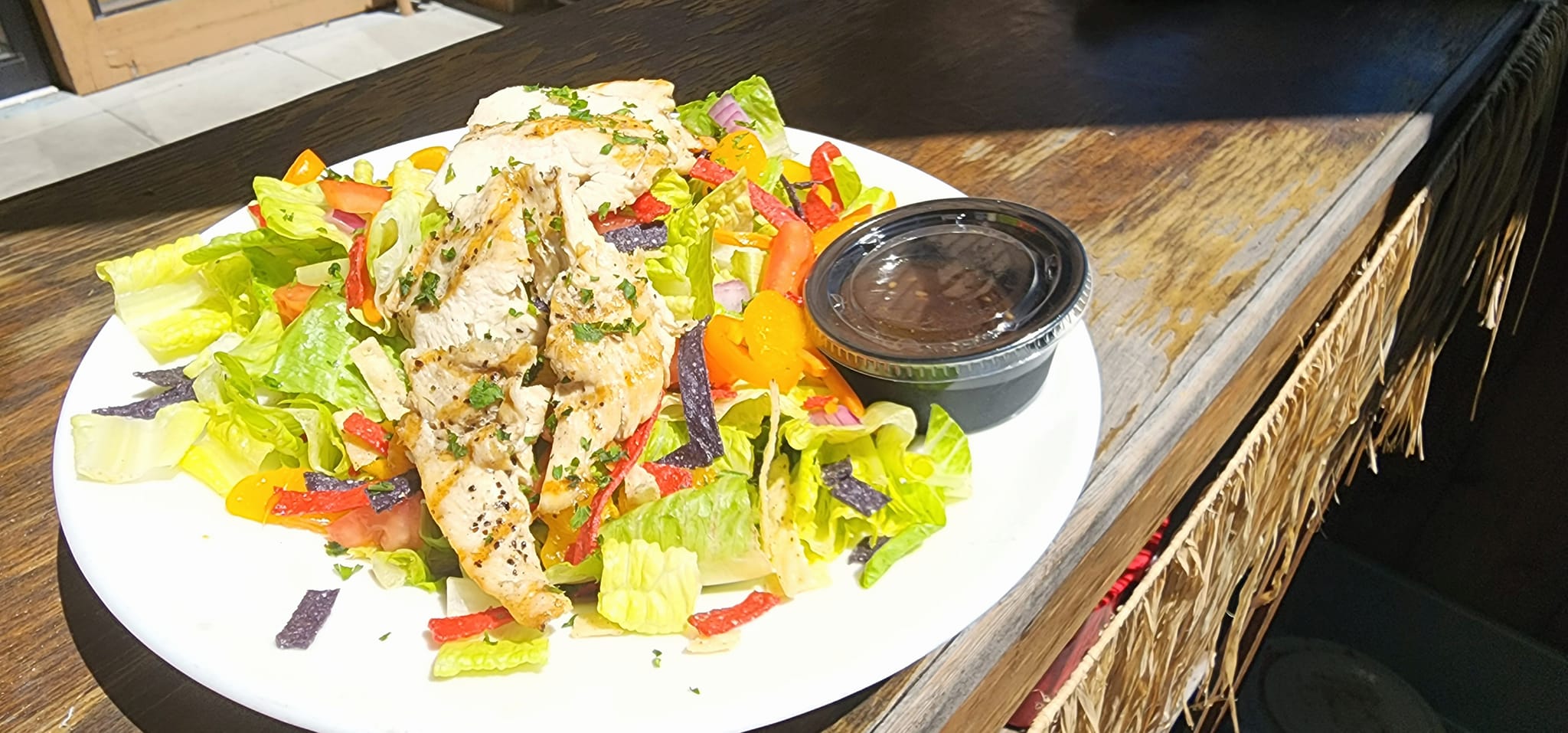 Grilled chicken salad with fresh vegetables and dressing on the side.