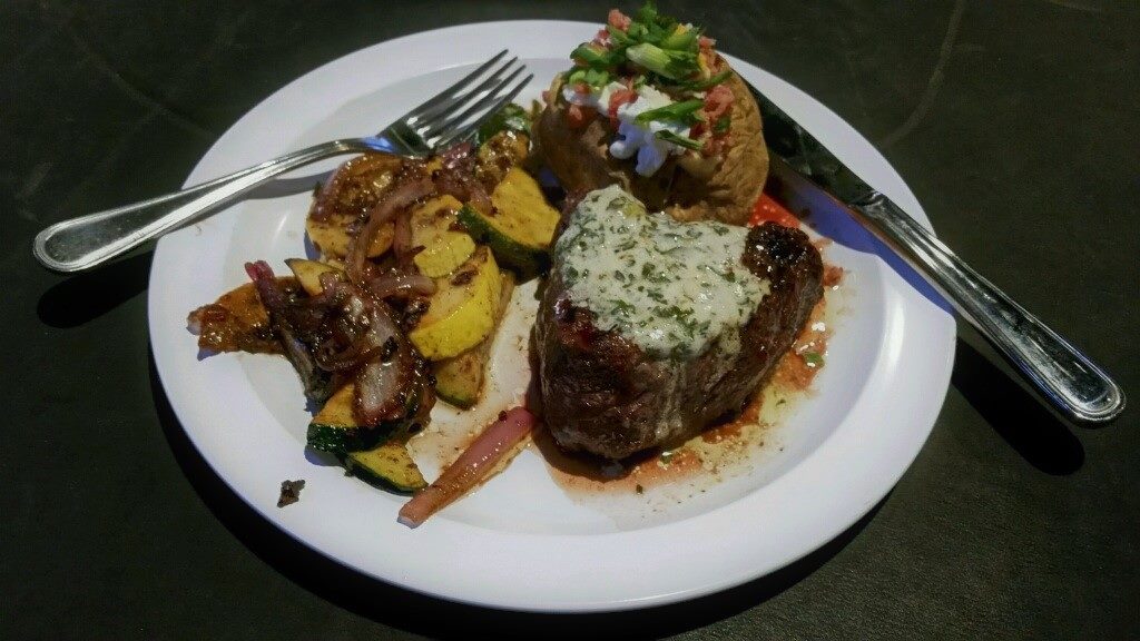 Grilled steak with herb butter and roasted potatoes on a white plate.