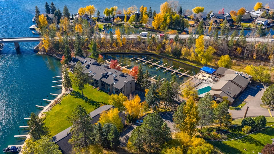 Aerial view of a lakeside residential complex with docks, clubhouse, and fall-colored trees along the water.