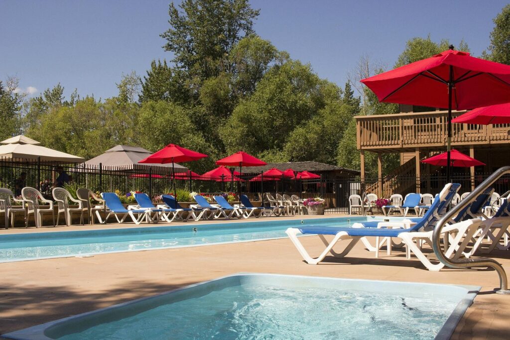 Outdoor pool area with lounge chairs and red umbrellas under clear skies.